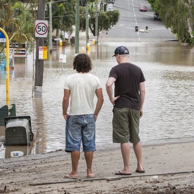 Men looking at flood water across road. Adobe